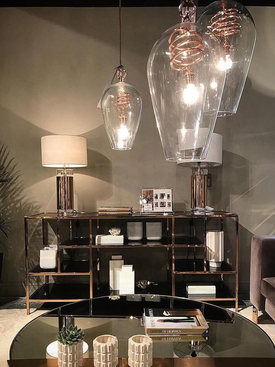 White-shade lamp on rear console beneath separate hanging glass pendants