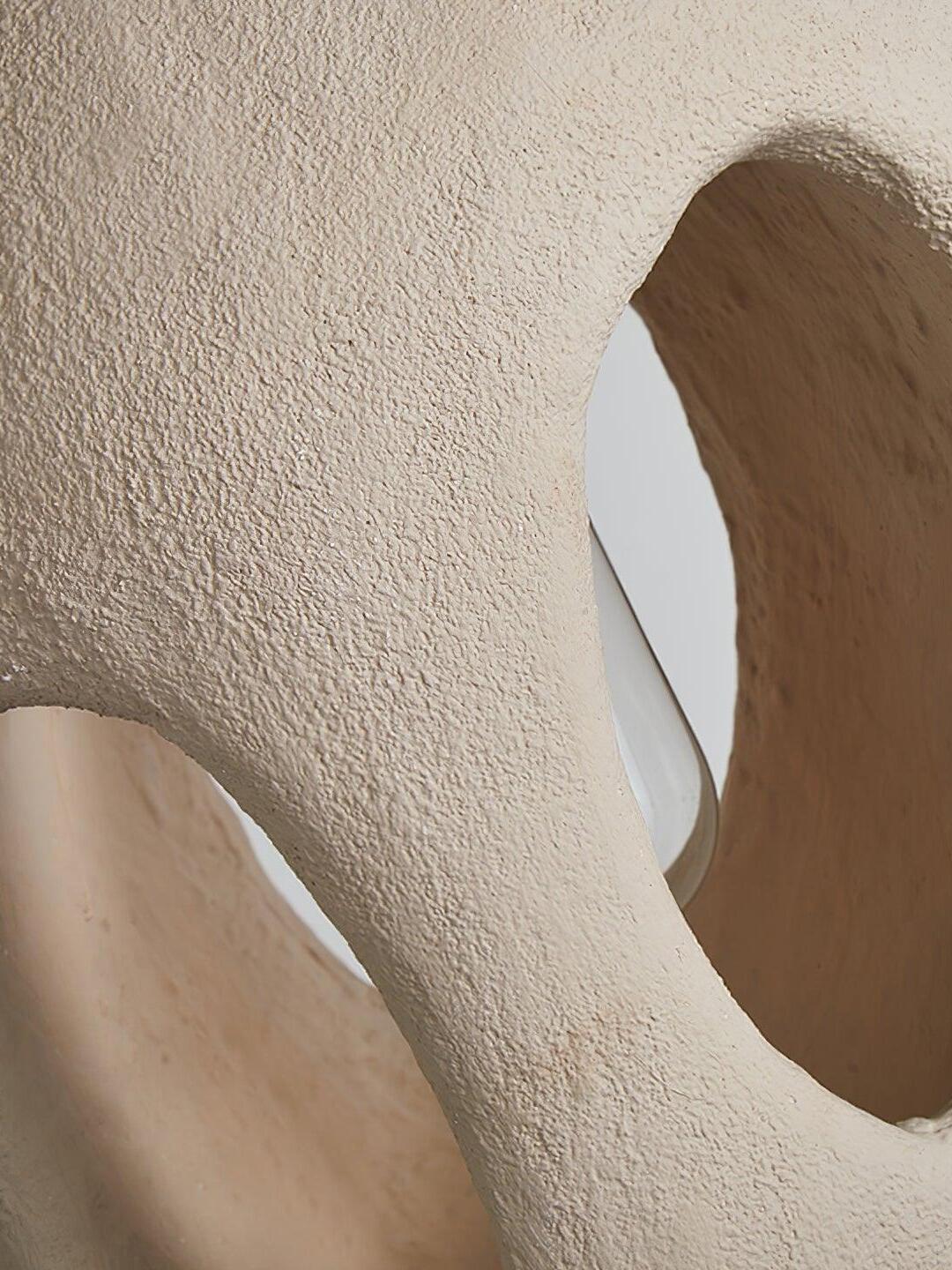 Macro view of a rough cream-looking surface and thick irregular rims around two unlit through-openings