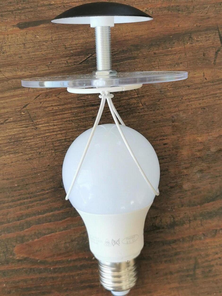 Detached frosted bulb with screw base, wire shade support, clear disk and black cap on wood
