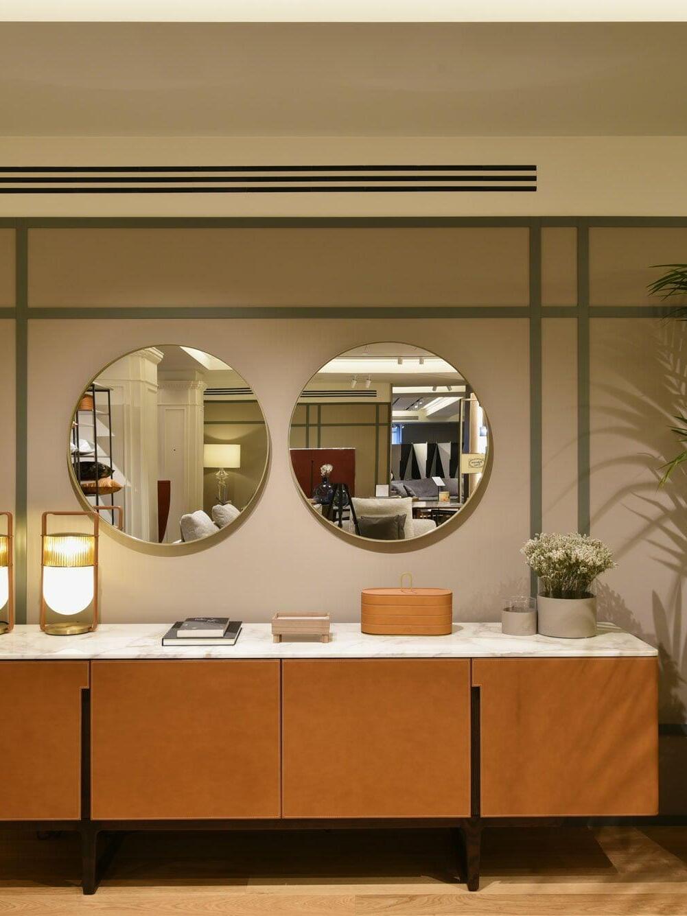 Wide room view with an illuminated Xi lamp at the left end of a sideboard beneath two round mirrors