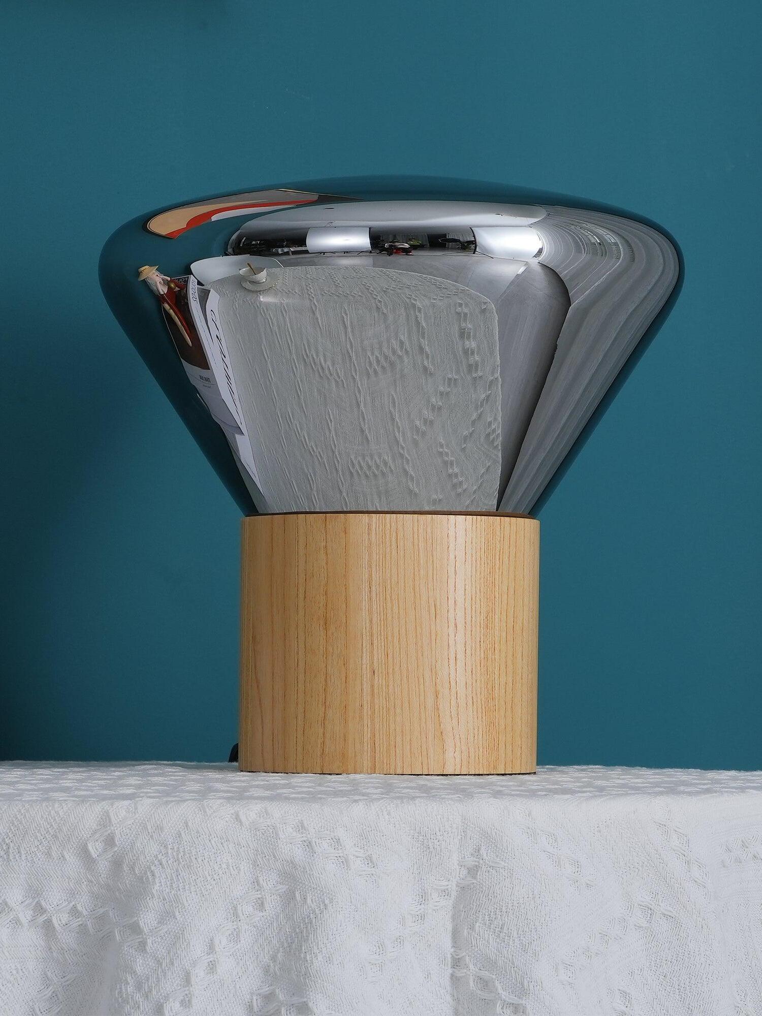 Unlit reflective smoky glass shade on light wood base against teal wall