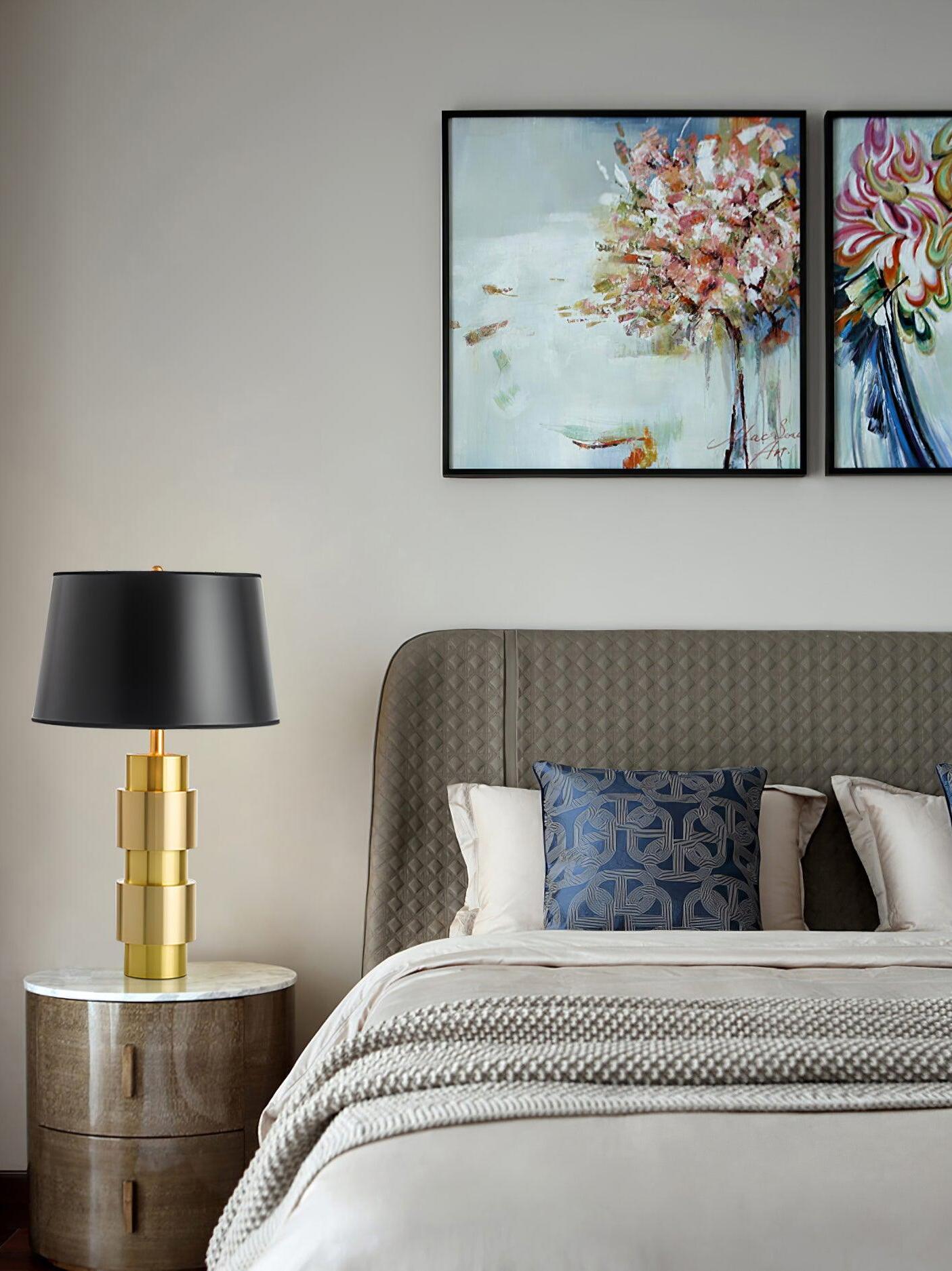 Jean lamp on a round bedside table beside a patterned headboard, blue cushion and floral artwork