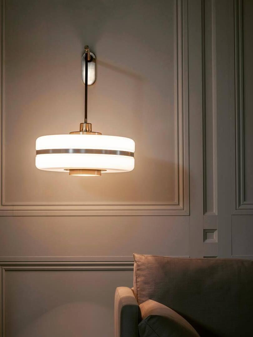Lit banded drum shade above chair on dark panelled wall