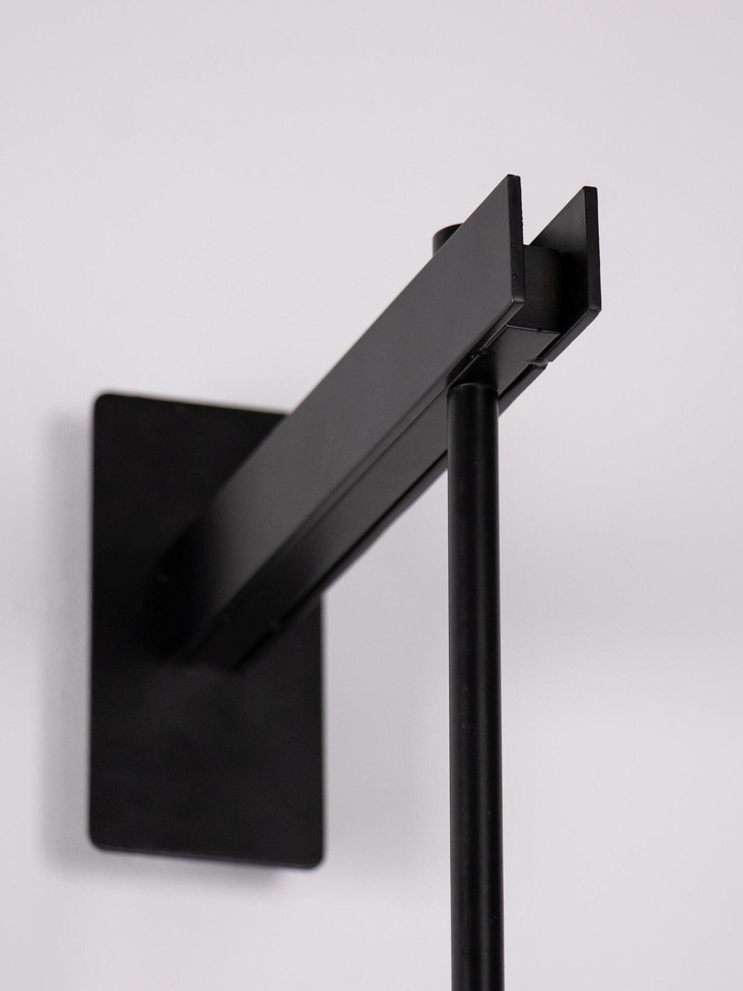Angled view of a black wall plate and rectangular upper bracket holding the vertical rod