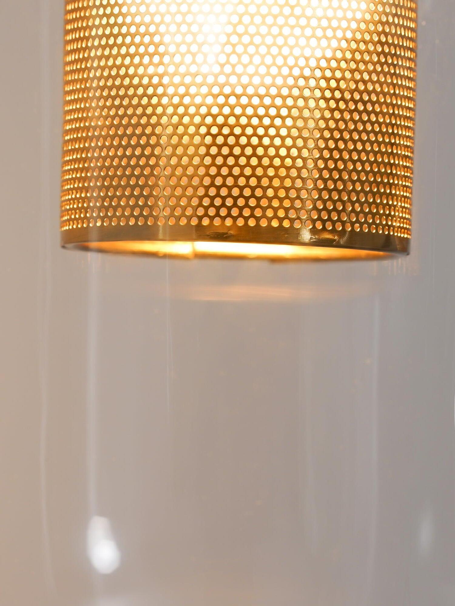 Close-up of the lower rim and fine perforations of a gold-tone cylinder inside clear glass
