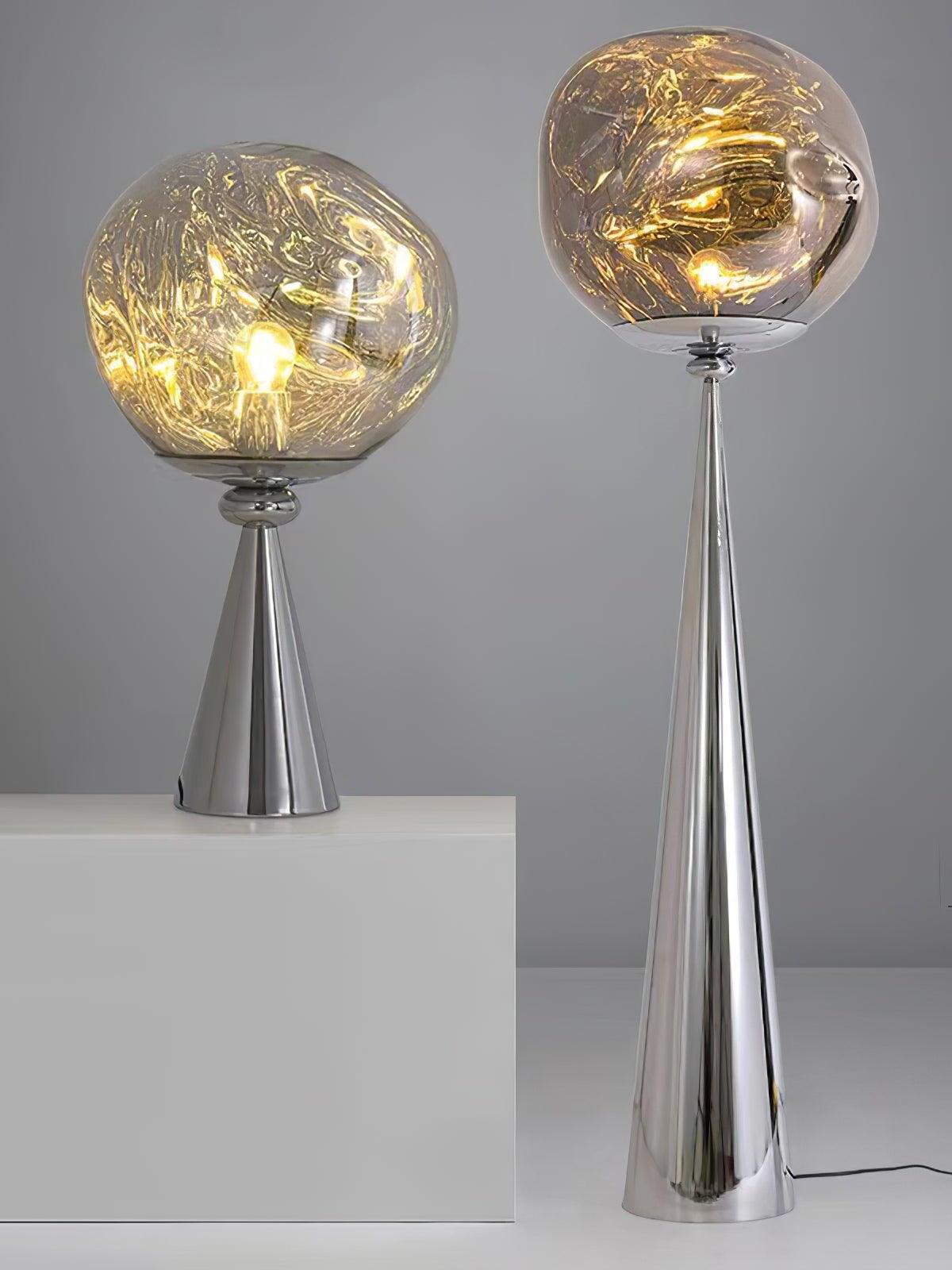 Glowing chrome globe table lamp on a white block beside a tall cone-base floor lamp
