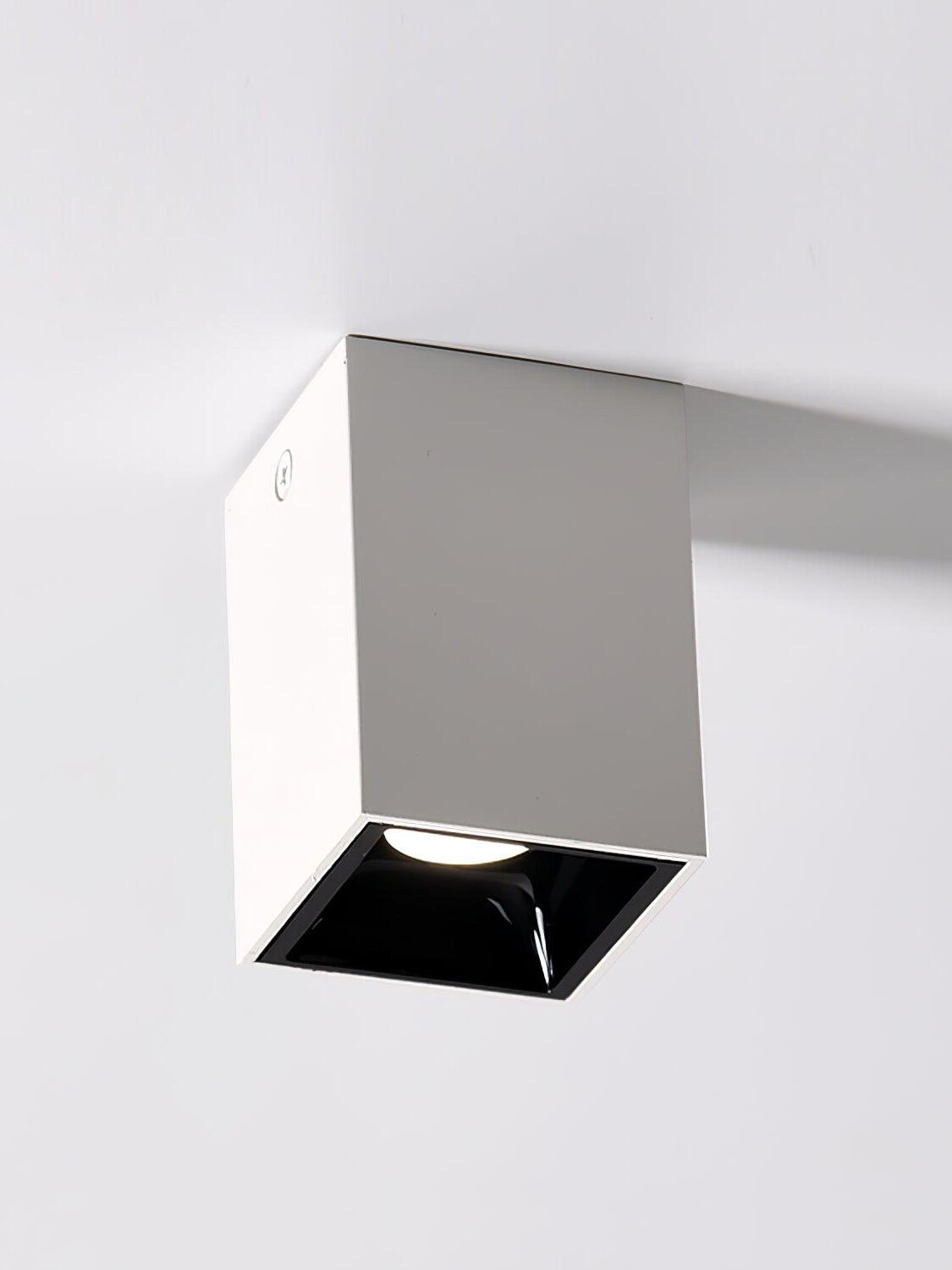Low view of a white ceiling spotlight with a glowing circular aperture, black recess and side screw