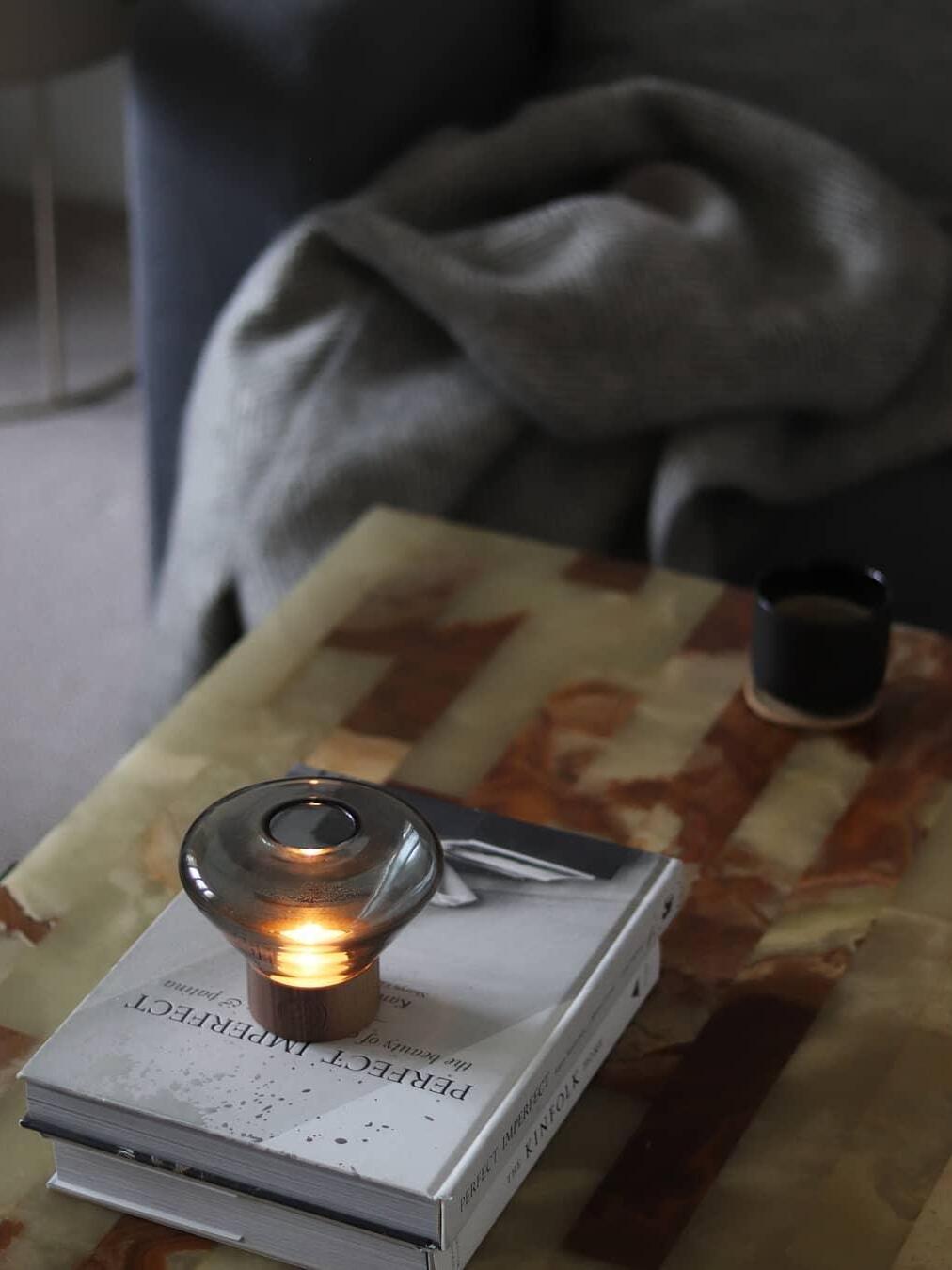 Small smoky rounded glass lamp glowing on books near upholstered seating