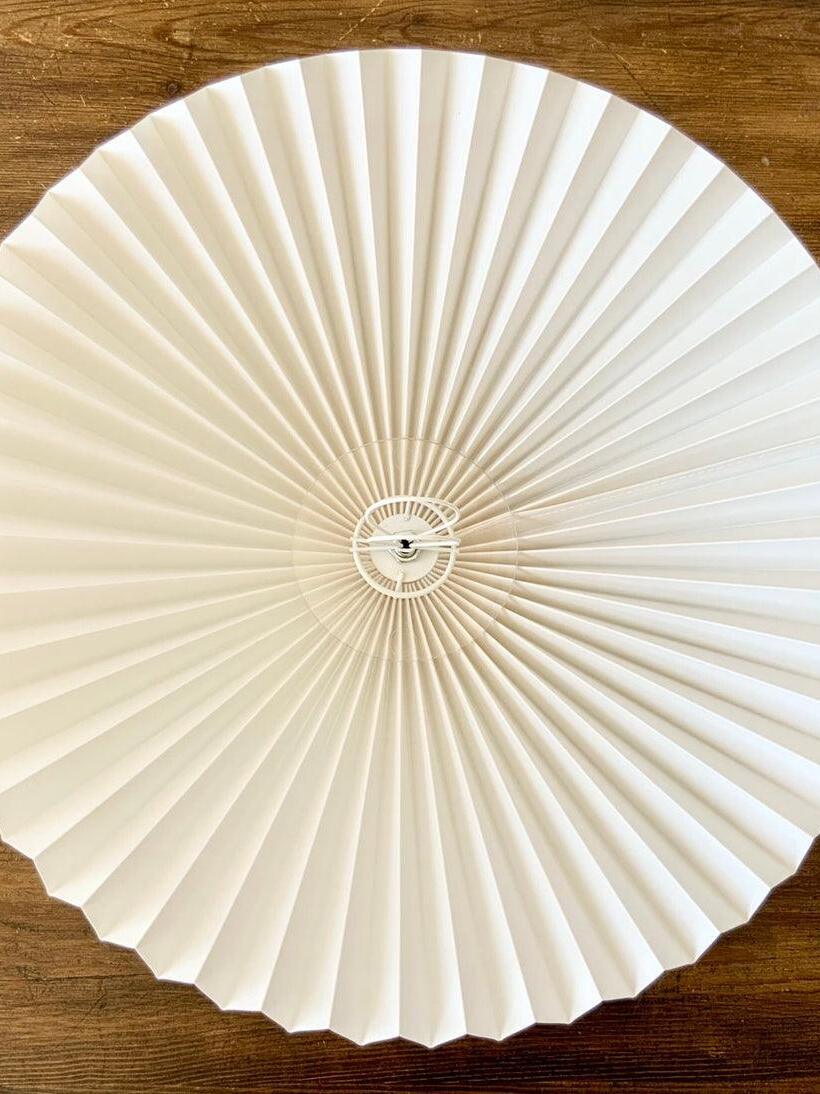 Underside of a pale pleated shade showing radial folds and circular support rings