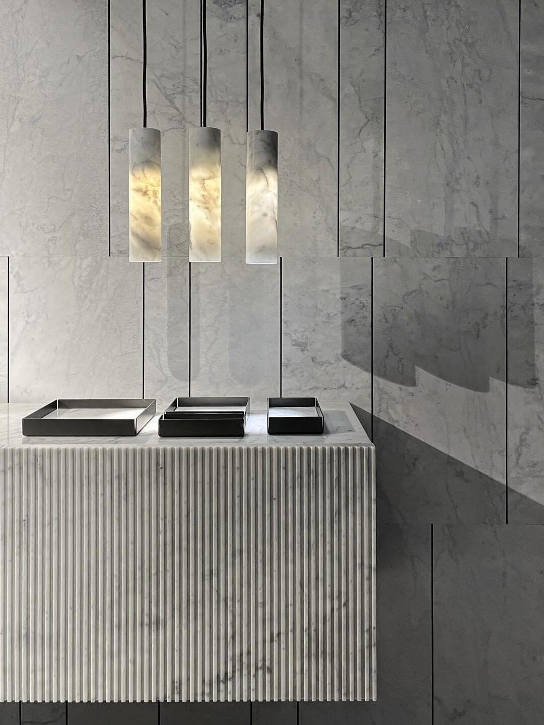 Three illuminated Silo cylinders above a ribbed cabinet against a grey stone wall