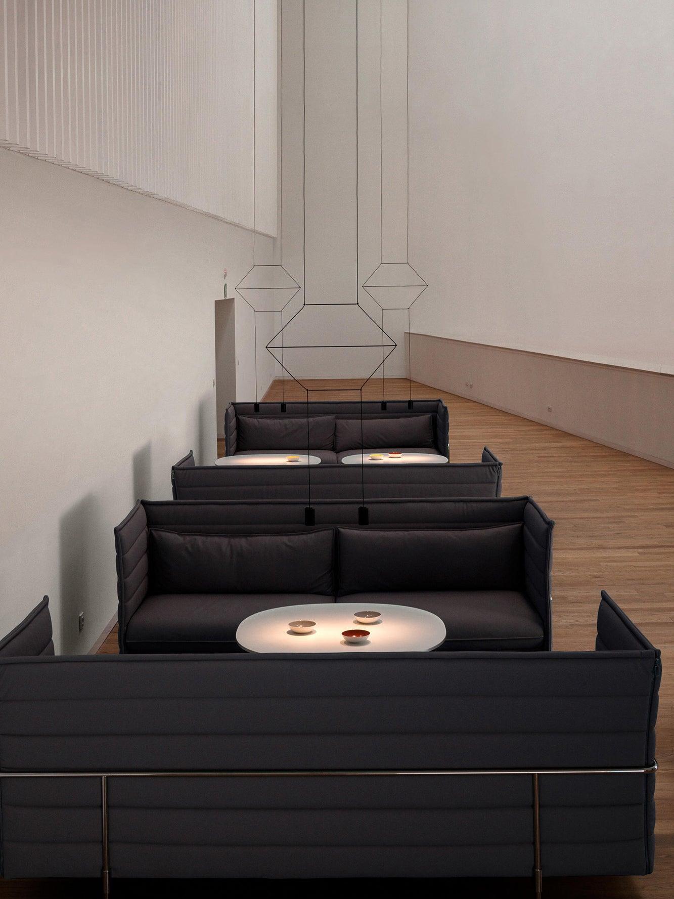 Diamond-shaped suspended wire arrangements with small black heads above dark sofa booths