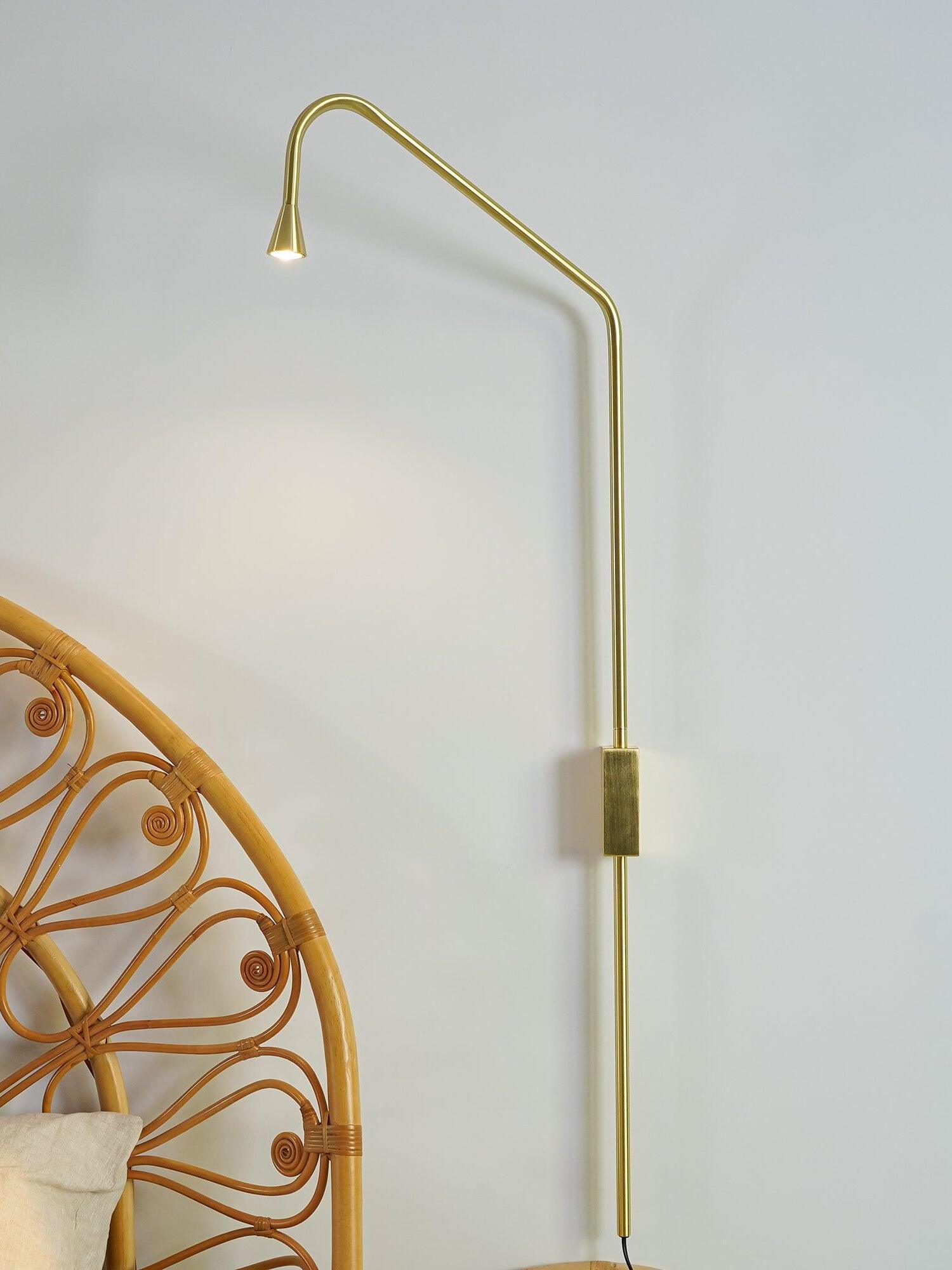 Golden slim wall light above a woven headboard