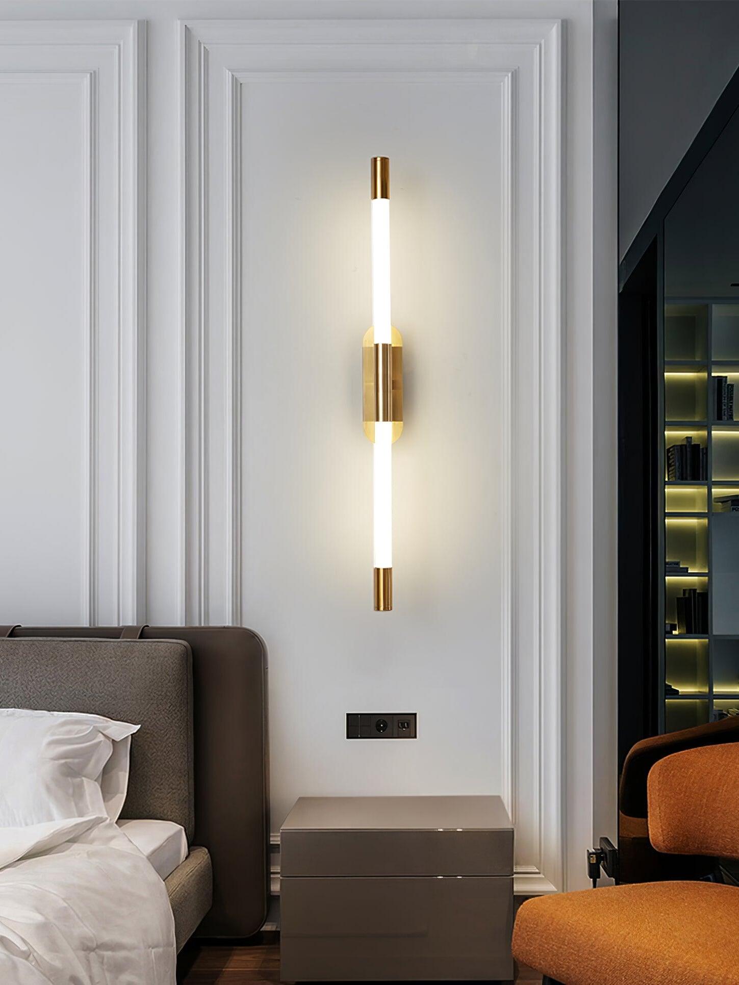 Gold Agnes wall light between a bed and tall curtains on a panelled wall