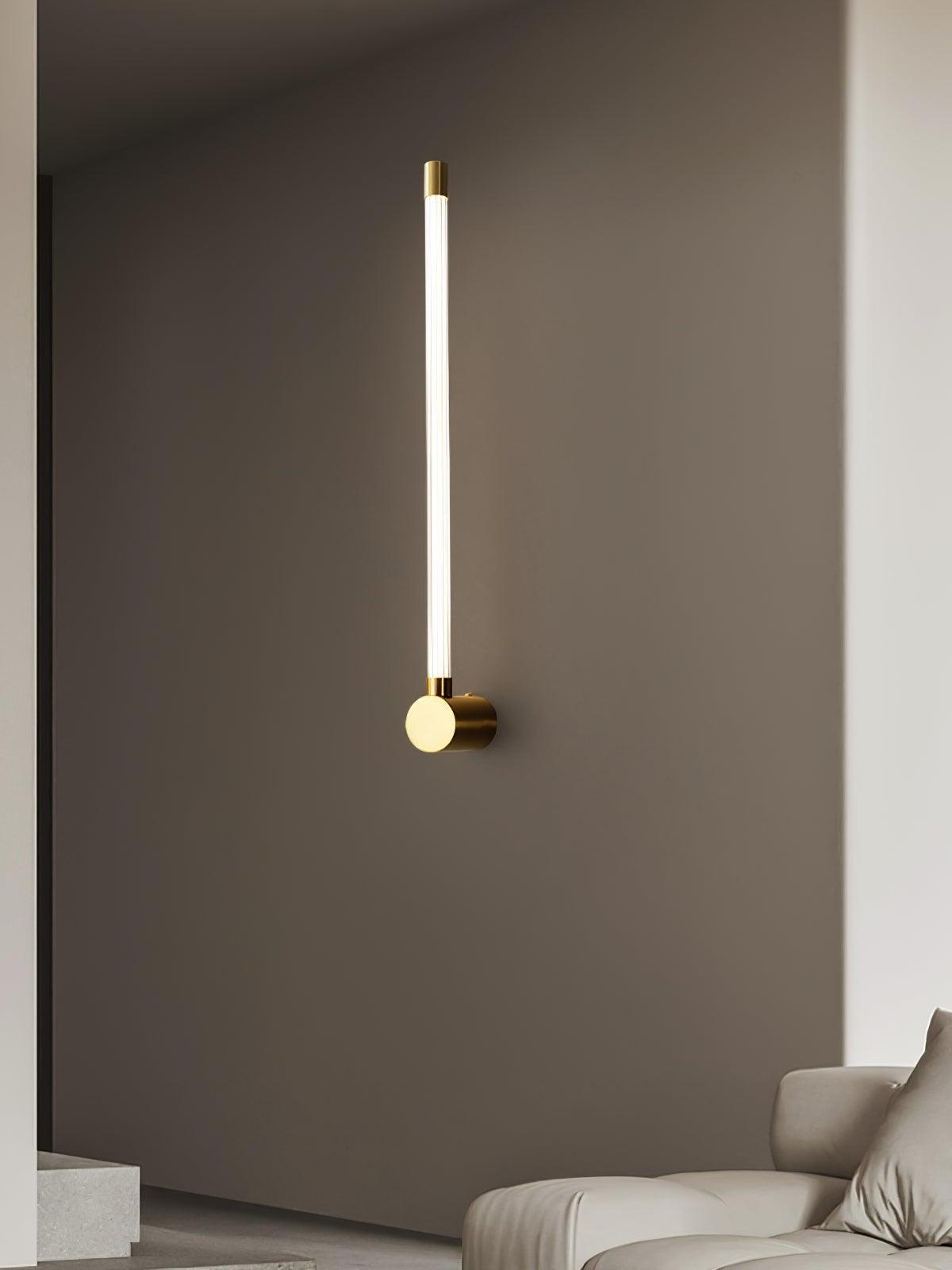 Brass-tone single-tube wall light glowing beside a pale sofa and stone steps