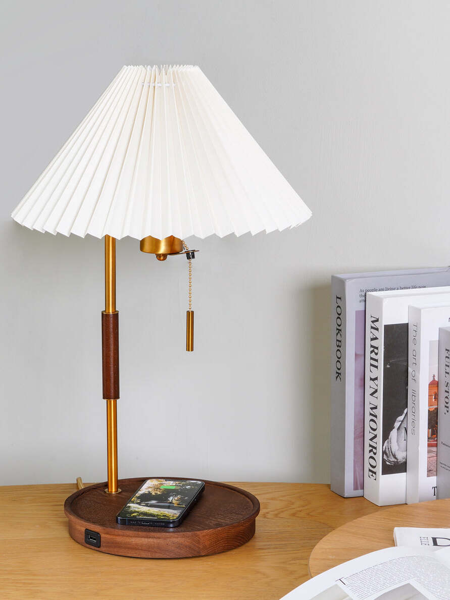 Front view of the white pleated table lamp with a phone on the wooden base beside books