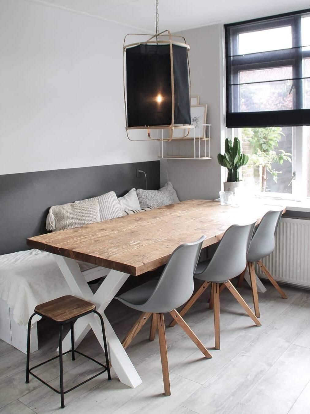 Black fabric lantern pendant above long wooden dining table and bench, with grey chairs, cactus and tall window