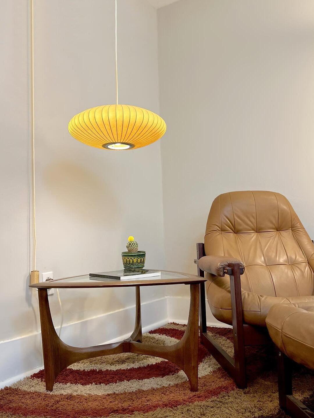 Glowing oval ribbed pendant above a glass-topped side table beside a leather chair