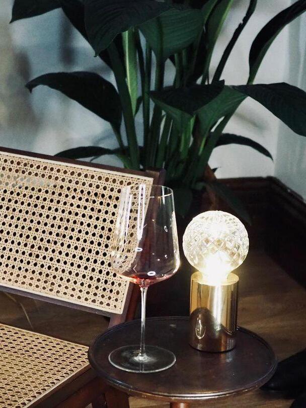 Lit patterned globe lamp beside wineglass and cane-backed chair