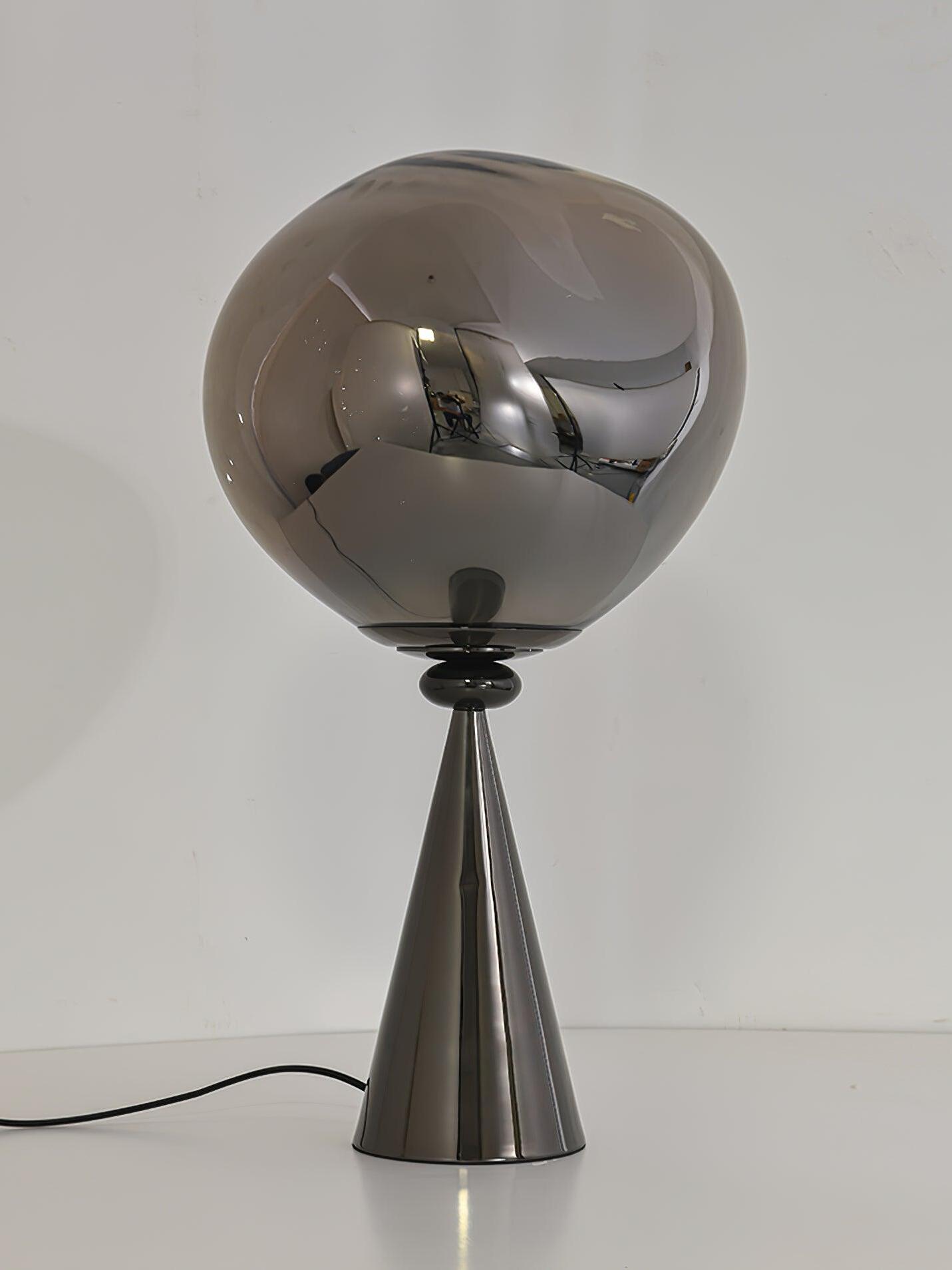 Unlit smoky globe table lamp with a reflective black cone base and cord on a pale background