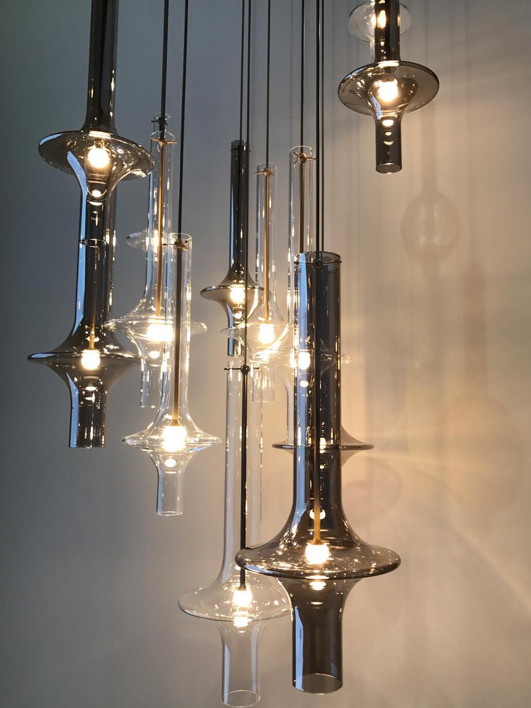 Cluster of lit clear and smoky flared glass pendants against a grey wall, with gold-tone and dark central stems