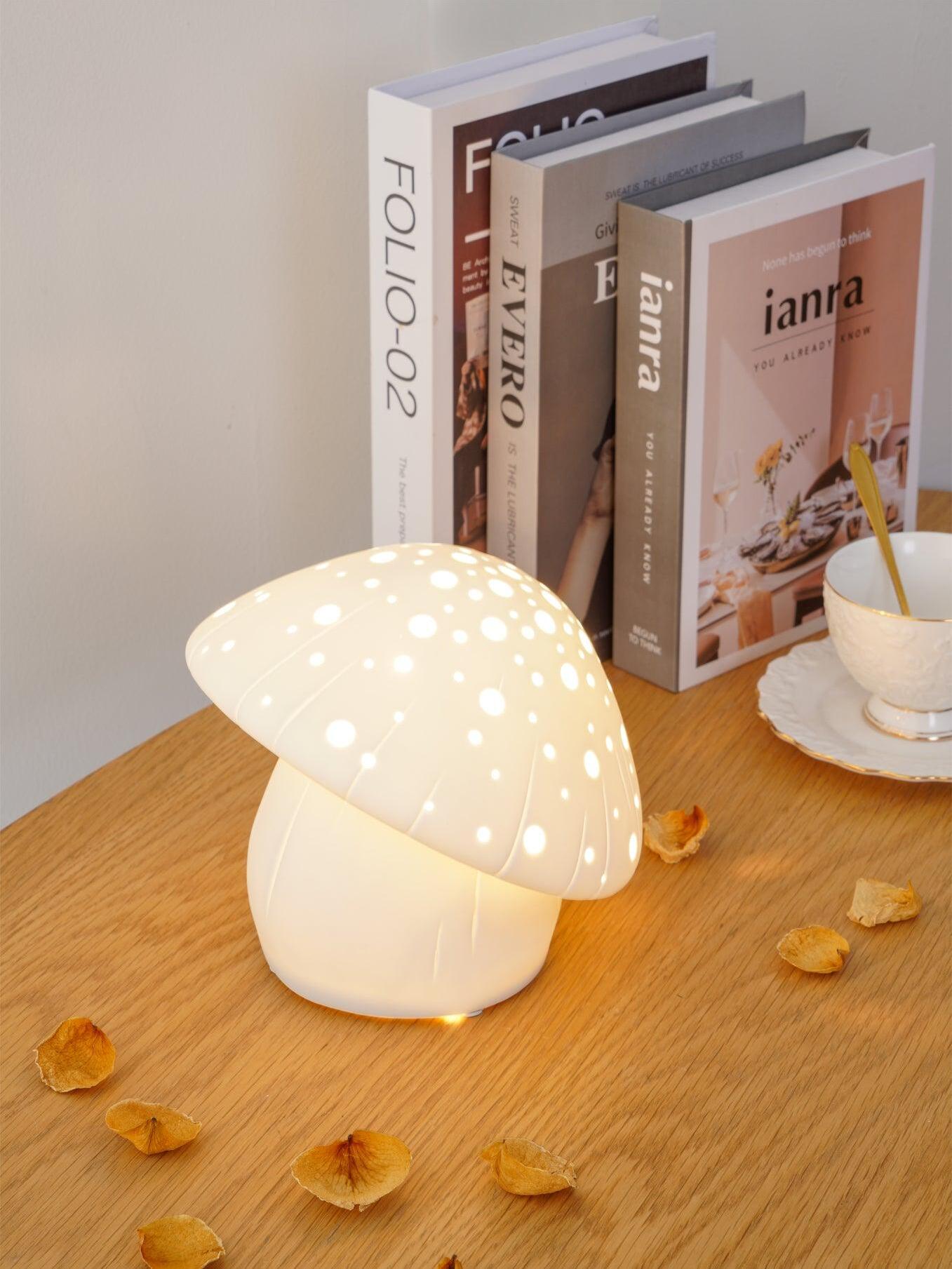 Illuminated Fungo lamp beside upright books and scattered petals on a wooden table