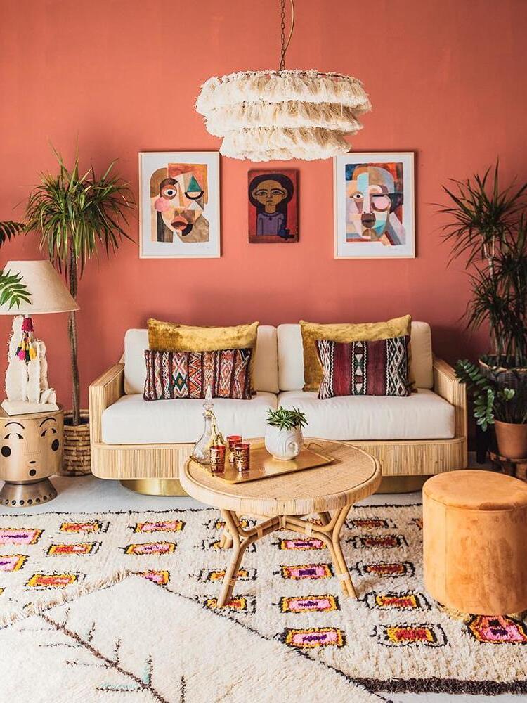 Cream tiered tassel chandelier above a cane sofa against coral walls, framed portraits and patterned cushions