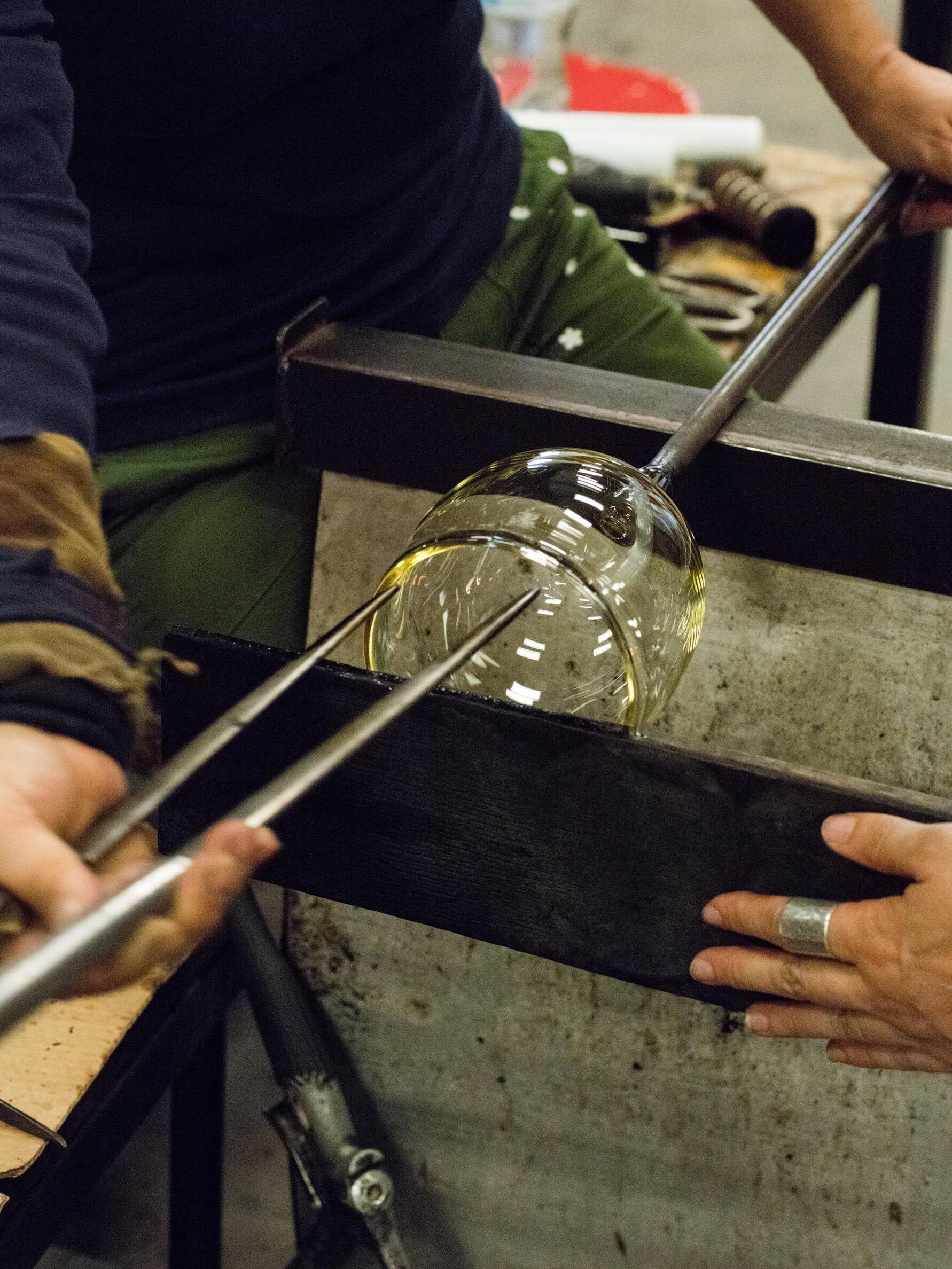 Glassworking photograph showing a transparent glass form being shaped with tools