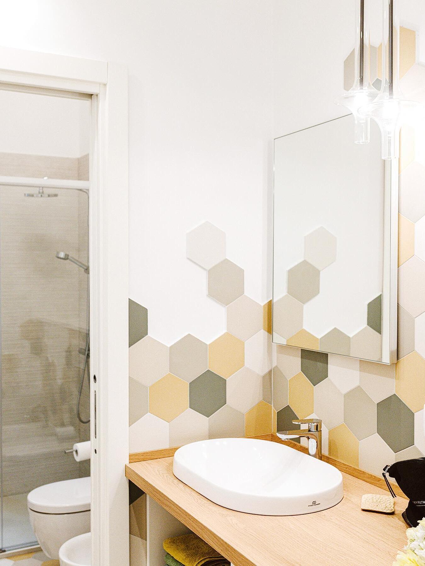 Two cropped clear glass pendants beside a bathroom mirror over a vessel basin, wood counter and hexagonal wall tiles