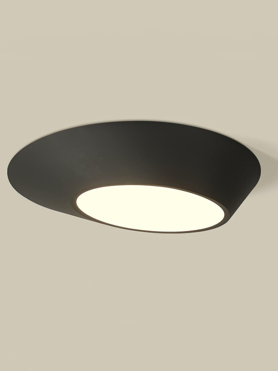 Close view of a black angled ceiling light with a warm-looking round diffuser on a pale ceiling