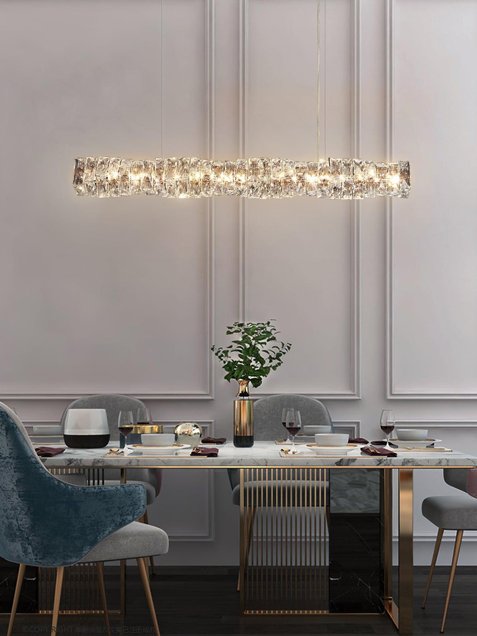 Linear crystal pendant above a dining table with blue chairs against a white panelled wall