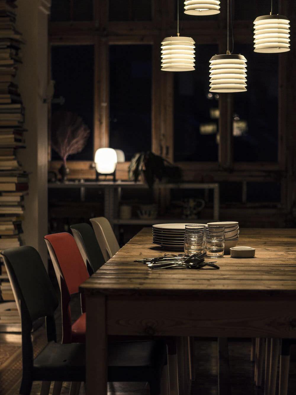 Group of lit layered pendants above long wood table in dark dining room