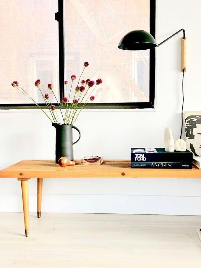 Black dome and angular arm on a wooden wall block above a slatted bench, vase of flowers and stacked books
