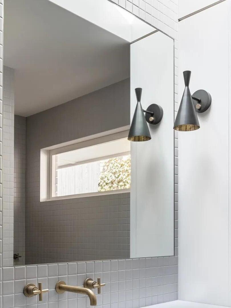 Two black cone wall lights reflected around bathroom mirror
