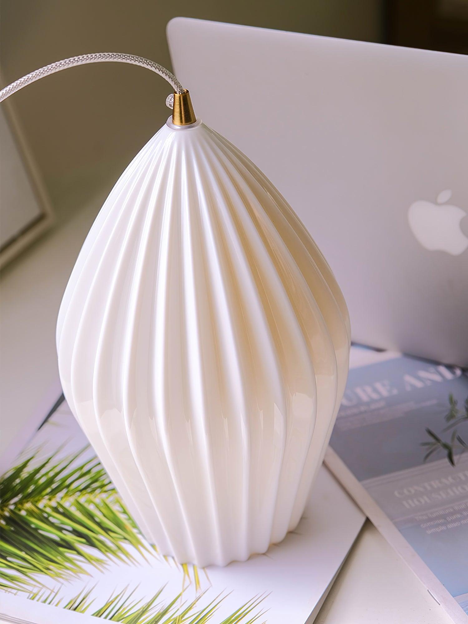 White ribbed ceramic shade resting on printed pages with its cord and gold-tone top fitting