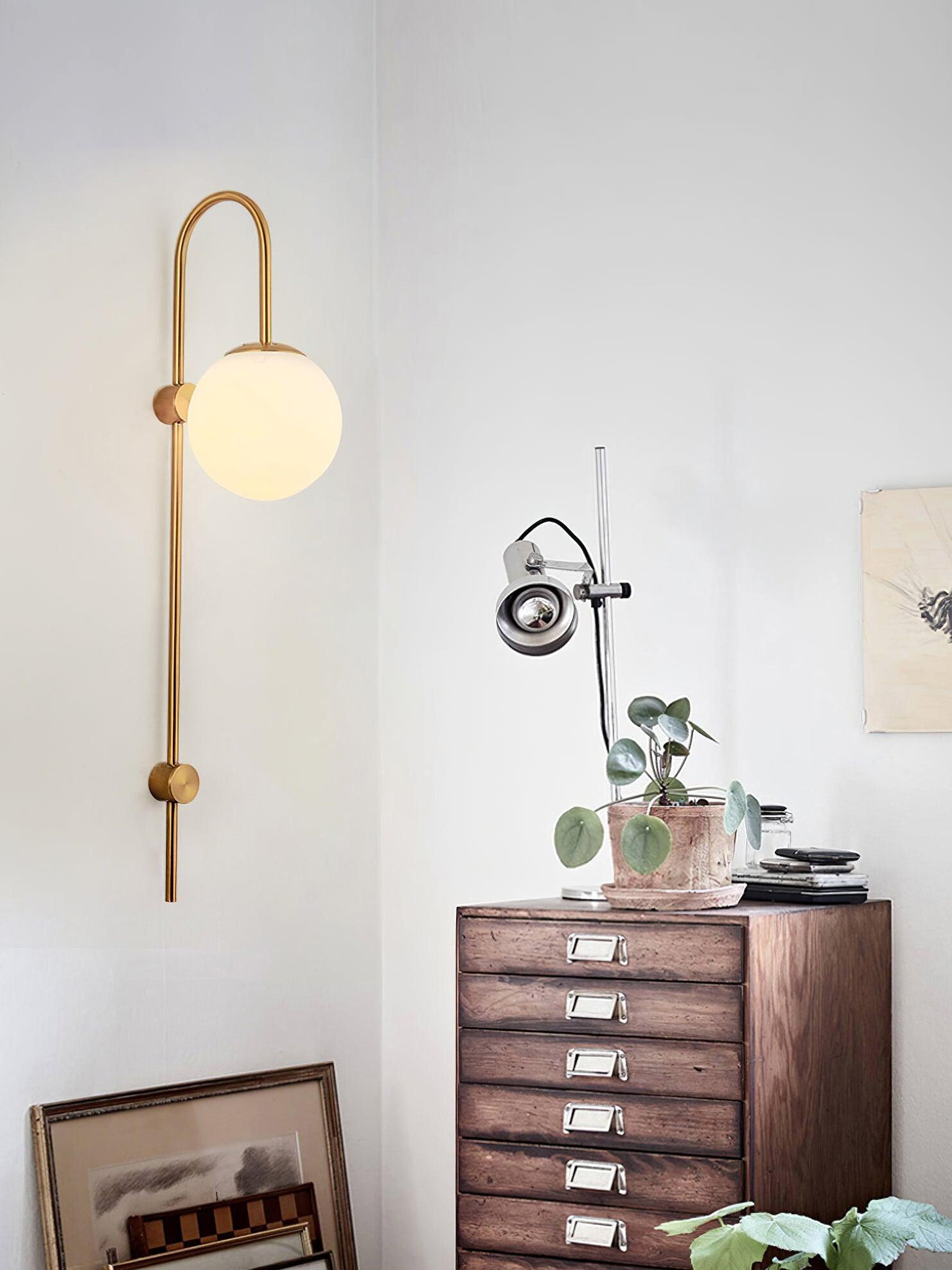 Gold wall light with curved top above wooden drawer cabinet