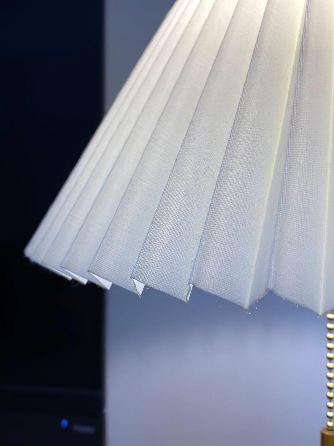 Detail of the white pleated shade edge with the pull chain at the right against a dark background