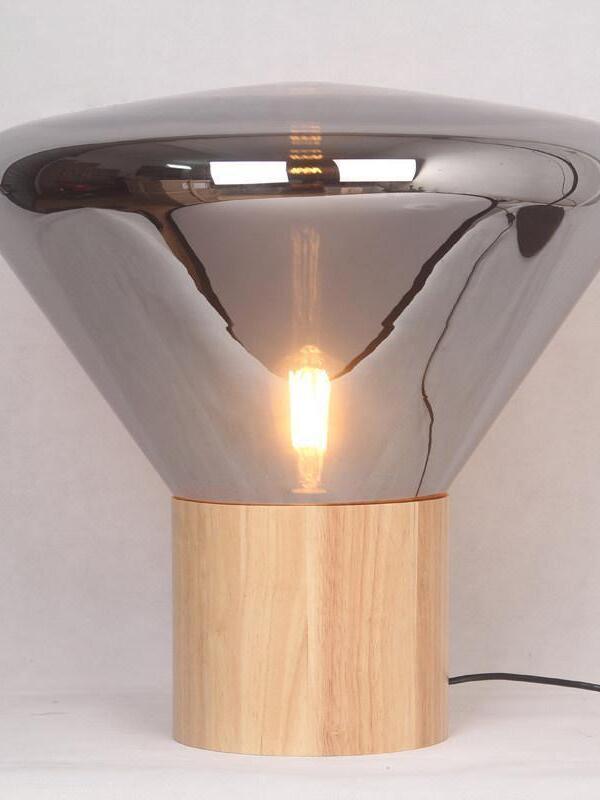 Reflective smoky flared shade and lit filament-style bulb above light wood base