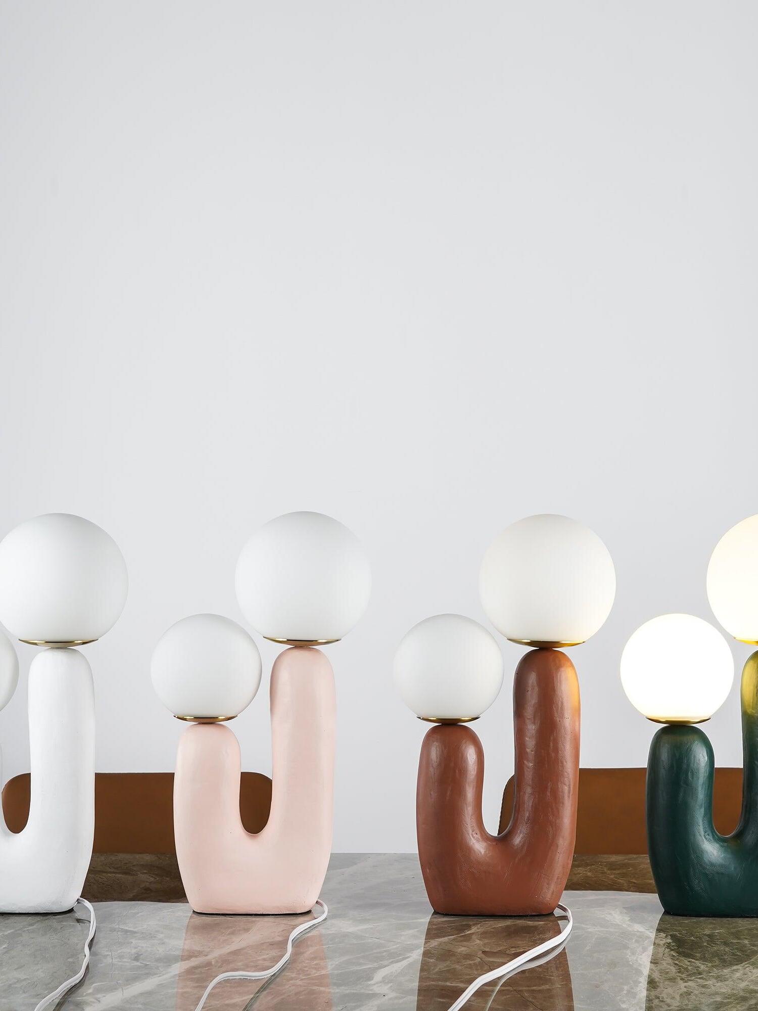 Row of white, pink, terracotta and green Oo Rough twin-globe lamps on marble, with white cords and brown chairs