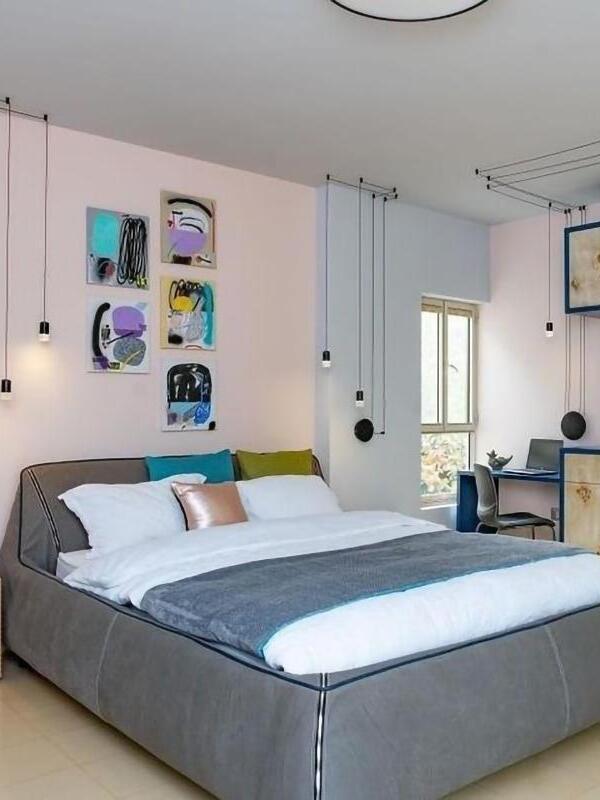 Black single-head cable pendants beside a bed with colourful artwork and pillows