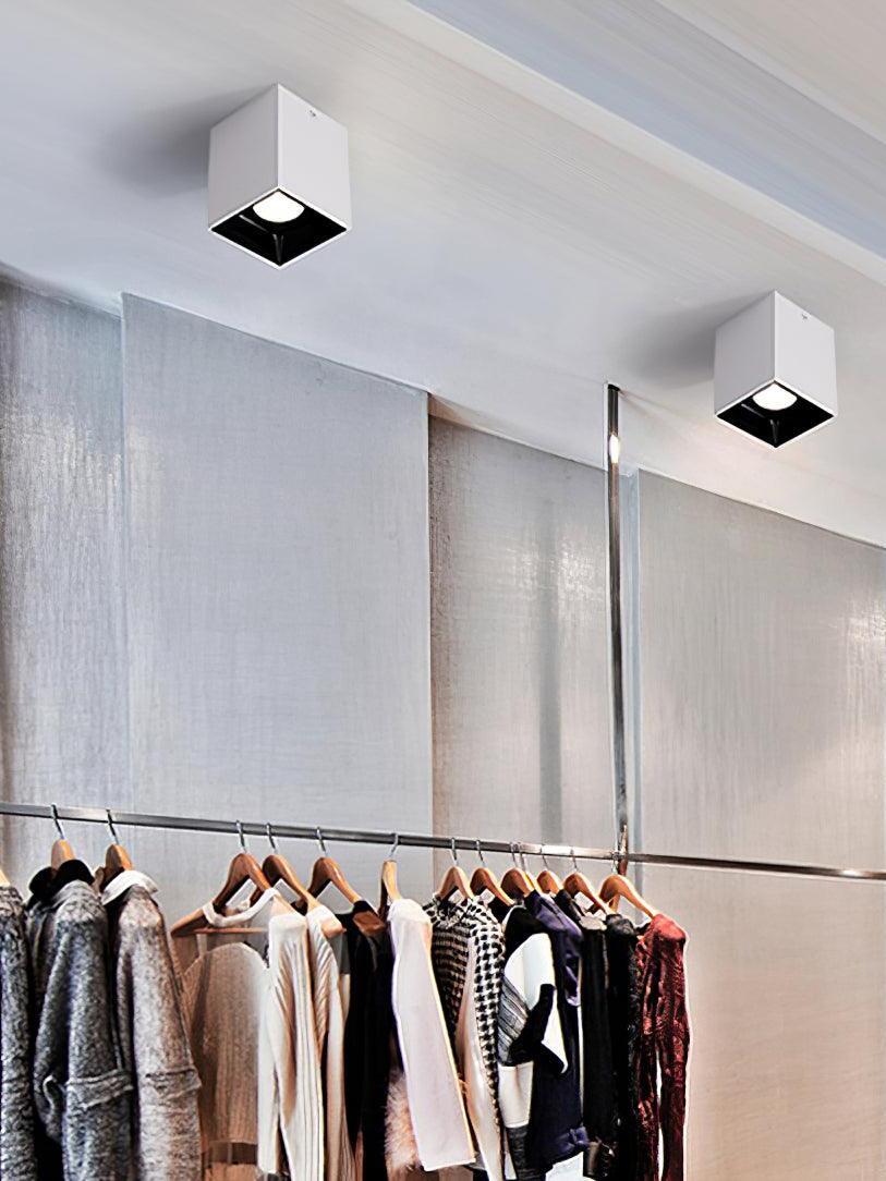 Two white ceiling spots above a clothes rail with shirts and tops on wooden hangers