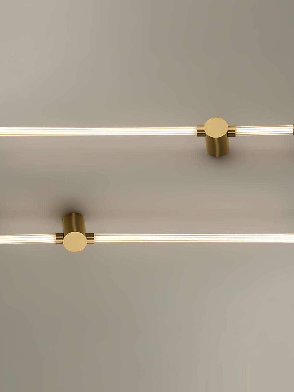 Two brass-tone long-and-short tube fixtures mounted horizontally at different positions on a pale wall