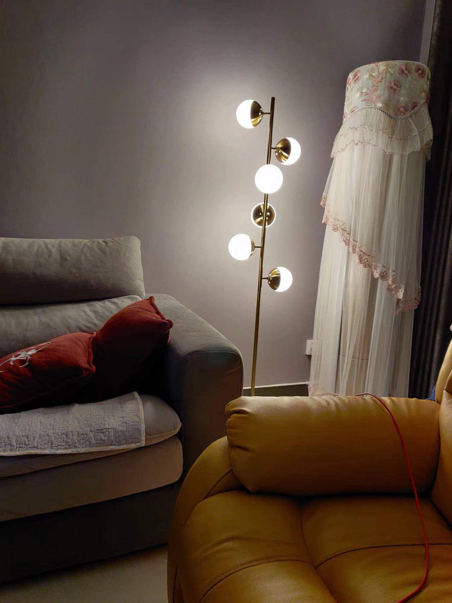 Gold globe floor lamp glowing by sofa and curtains
