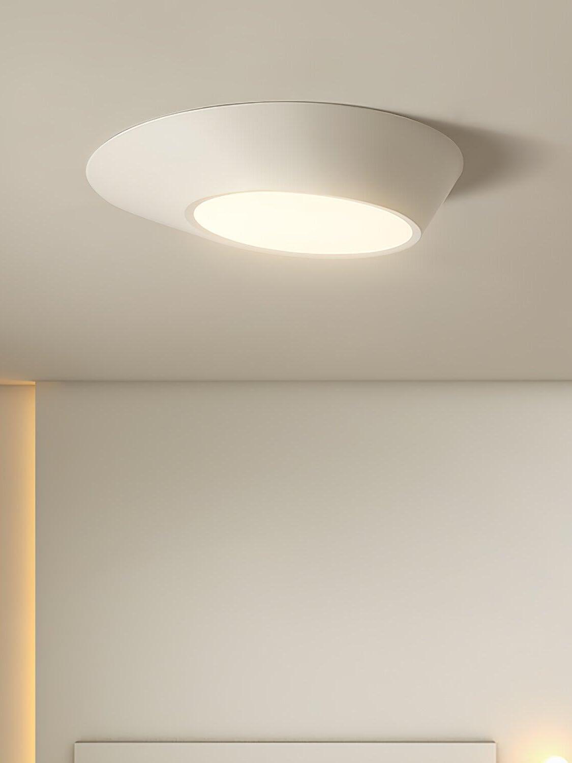 Close view of a glowing white angled ceiling light above a partial white bedhead