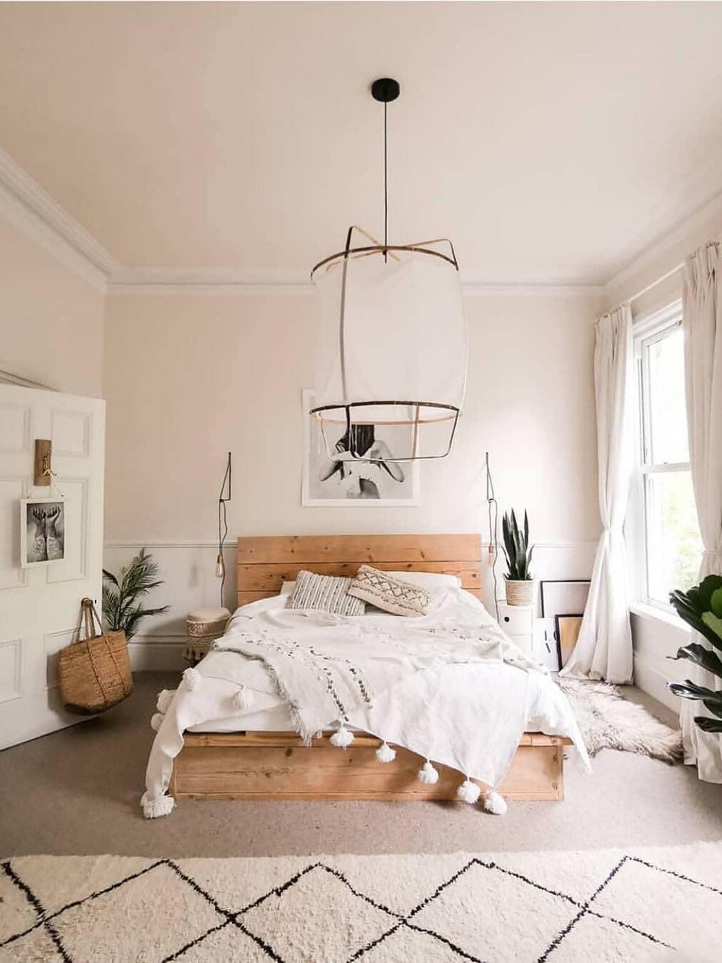 White lantern pendant above wooden bed with white bedding, long black cord and round black ceiling canopy