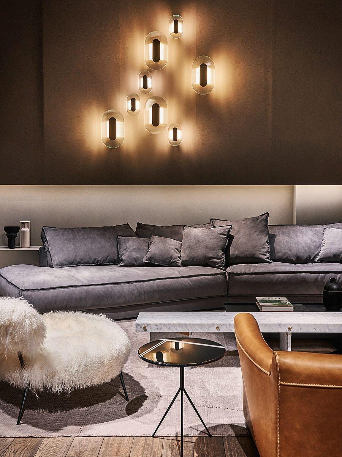 Elongated Button wall-light group above a grey sofa with white shaggy and tan chairs in the foreground