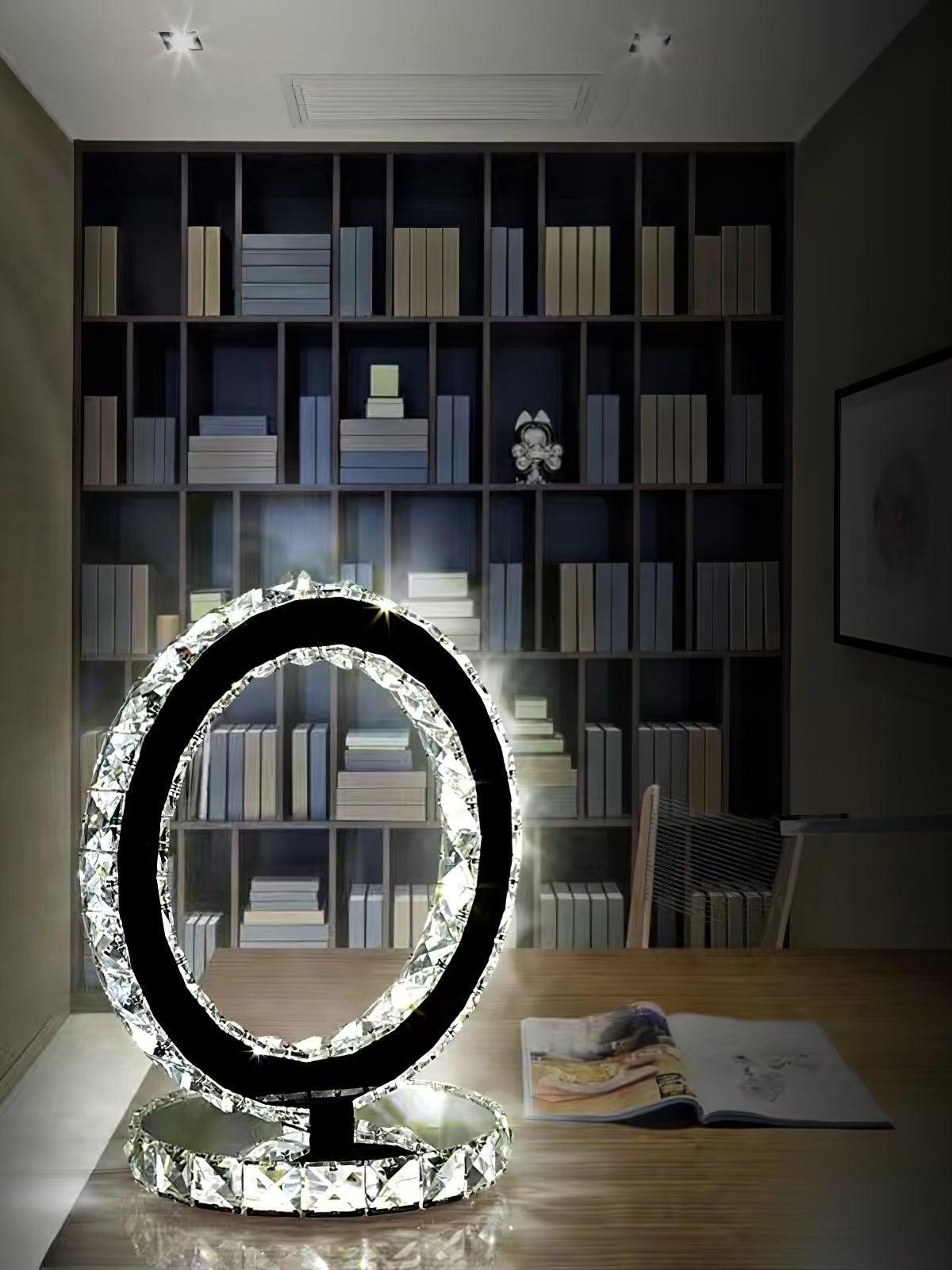 Ring lamp on a wooden desk beside an open book in front of shelving