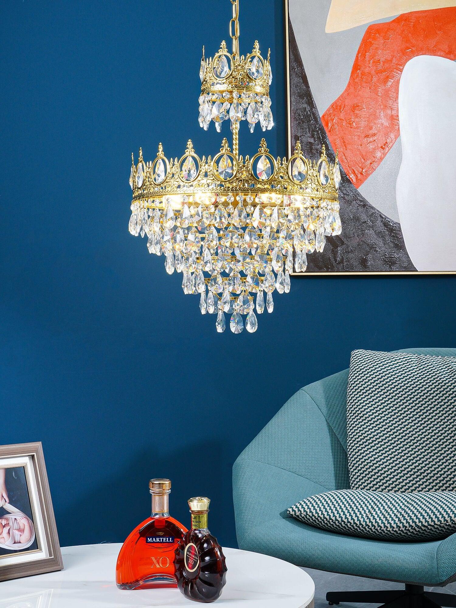Crystal chandelier above a white side table with bottles, a teal chair and abstract wall art