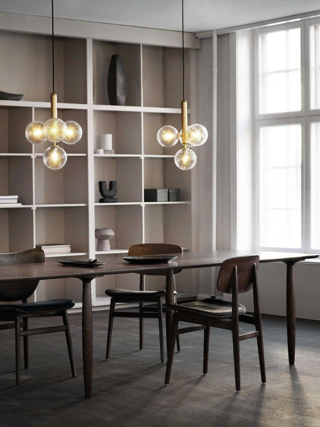 Two clear globe clusters on brass-colour stems over a dark dining table before cubby shelving
