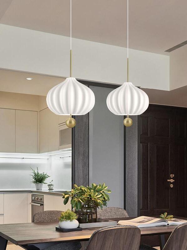 Two white fluted Lilli pendants with brass balls over a wooden dining table with plants and an open book