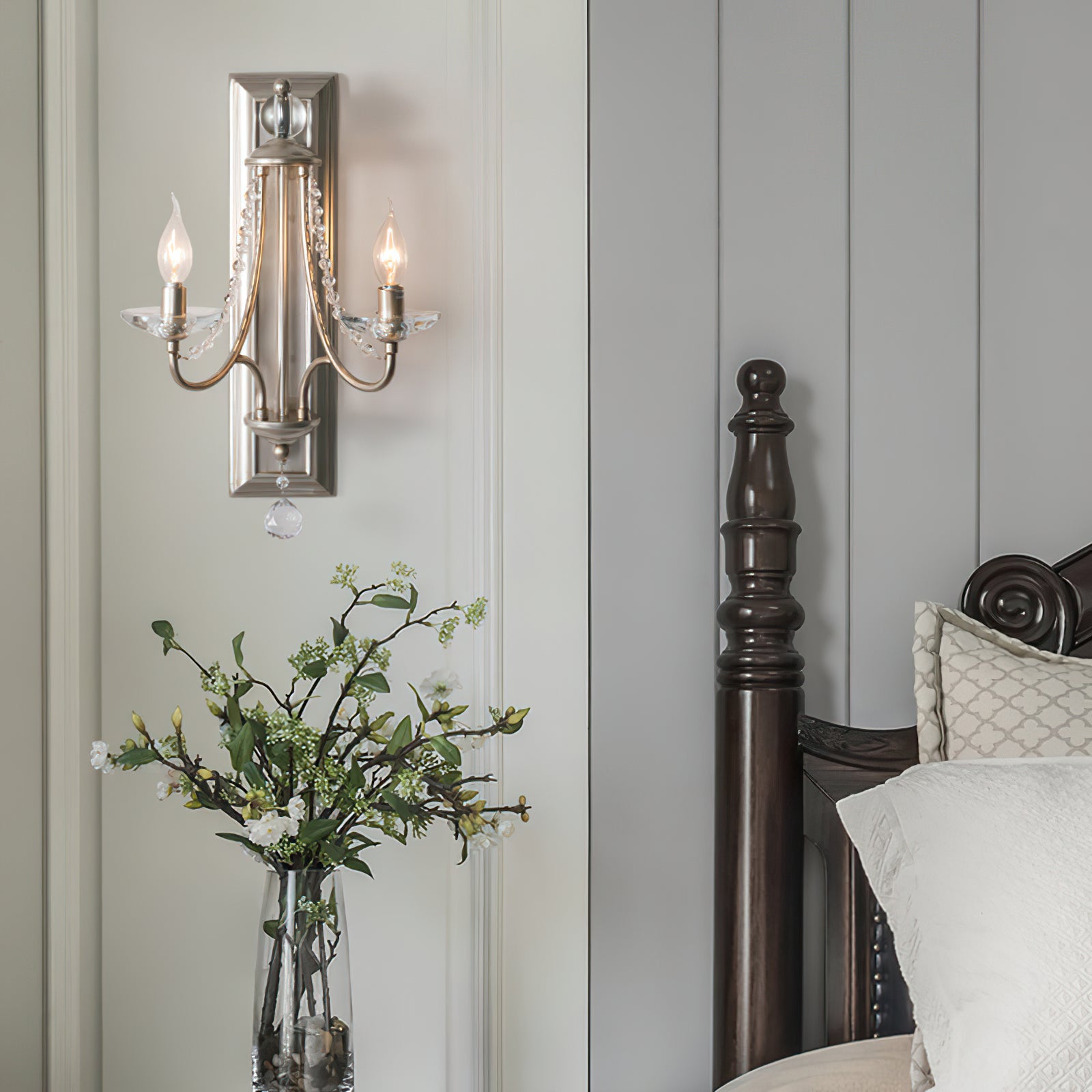 Silver two-arm wall sconce beside a bed and greenery